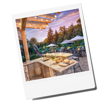 Elegant outdoor kitchen with a gazebo, featuring a barbecue grill, granite countertops, and seating area surrounded by lush landscaping.